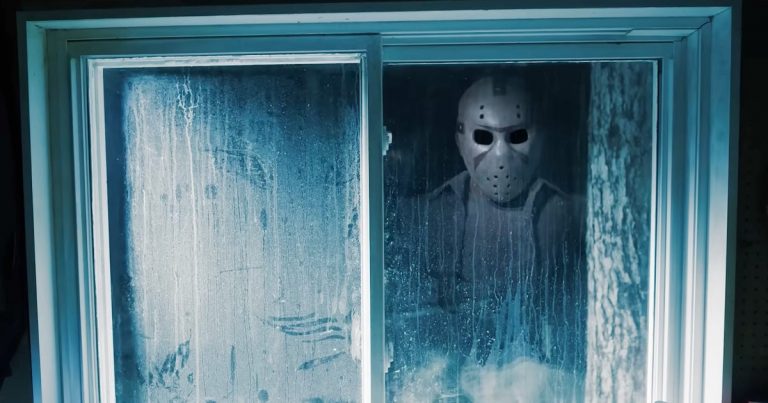 Screenshot-from-Dead-by-Daylights-Jason-trailer-showing-a-masked-figure-standing-outside-a-grimy-window-and-looking-into-a-room